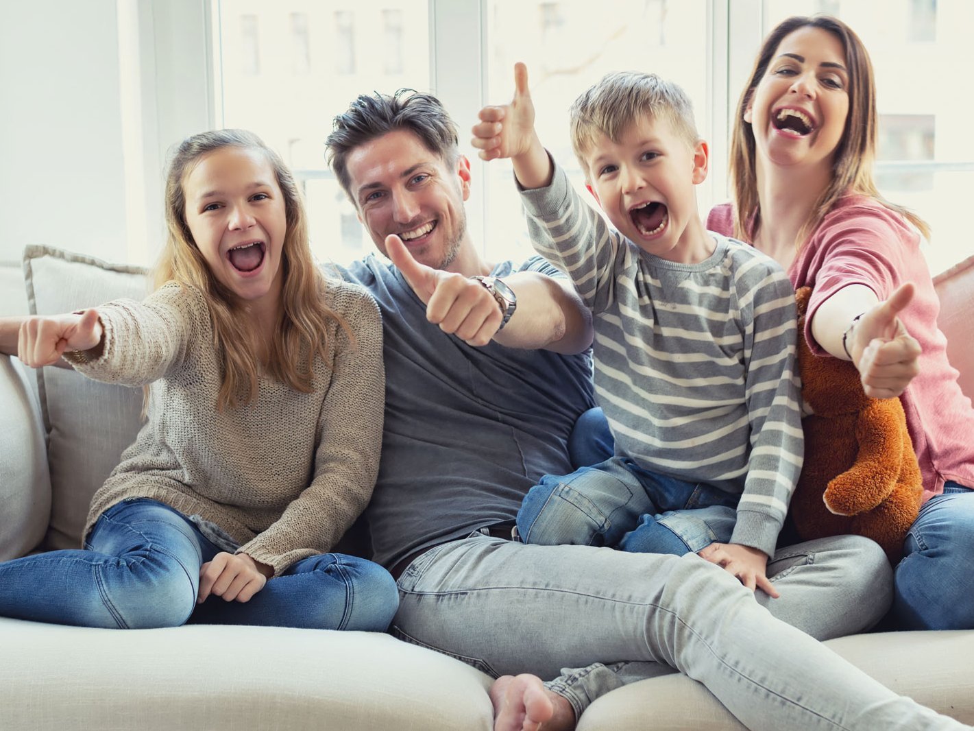 Eine Familie, die auf dem Sofa sitzt und die Daumen nach oben zeigt